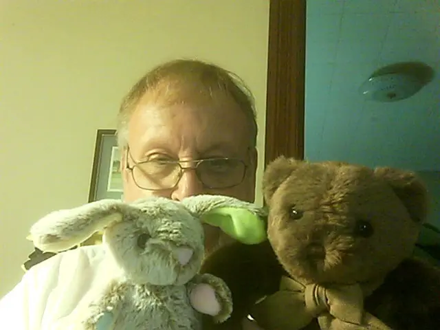 Man posing with a white stuffed rabbit and a brown teddy bear.