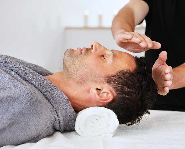 A man receiving a forehead massage while lying on a towel.