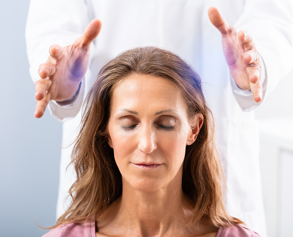A woman receiving a calming energy healing session with hands hovering above her head.
